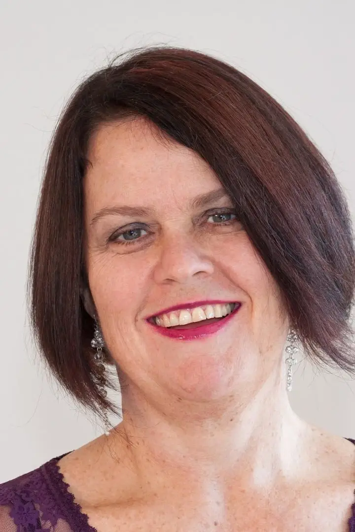 Lächelnde Frau mit braunen kurzen Haaren und pinkem Lippenstift und Glitzerohrringen.